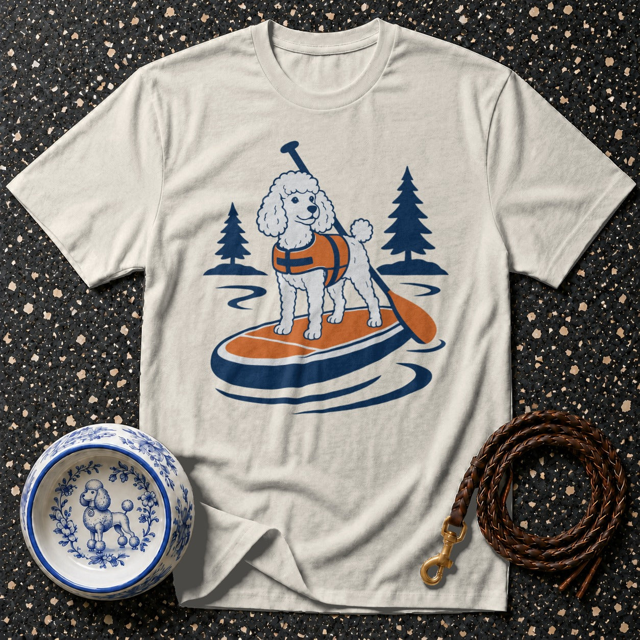 White t-shirt featuring a cartoon poodle paddleboarding with trees and water.