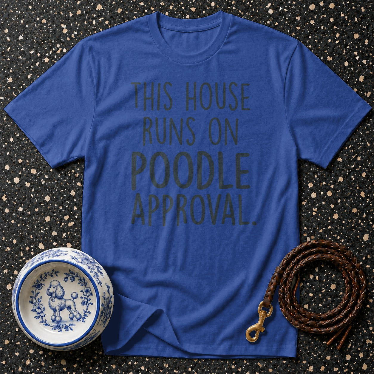 Blue t-shirt with text "THIS HOUSE RUNS ON POODLE APPROVAL." beside a poodle bowl and leash.