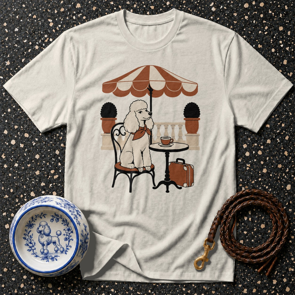 Cream t-shirt with a poodle sitting at a table under an umbrella.