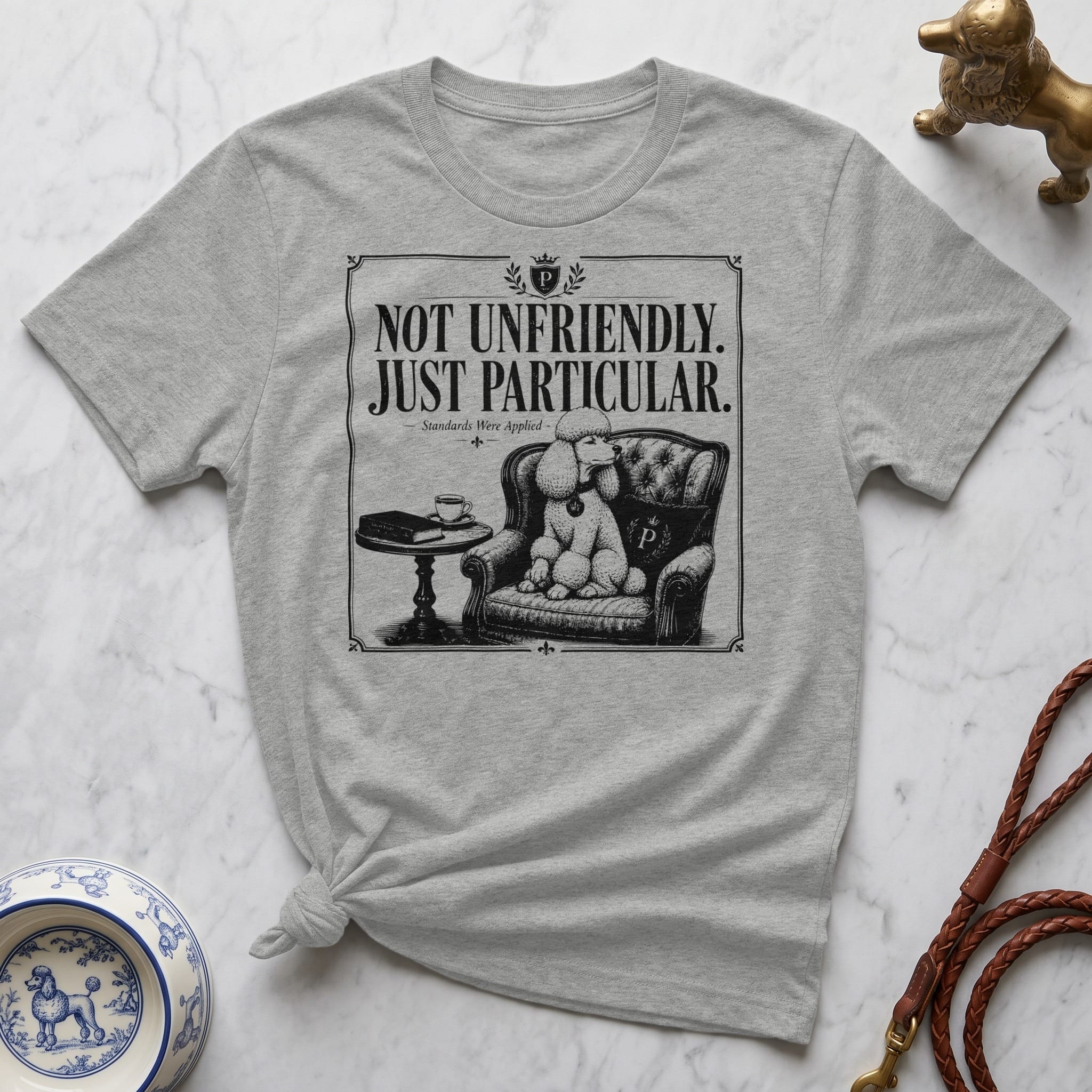 Grey t-shirt with black illustration of poodle sitting in chair, "Not Unfriendly. Standards Were Applied." text.