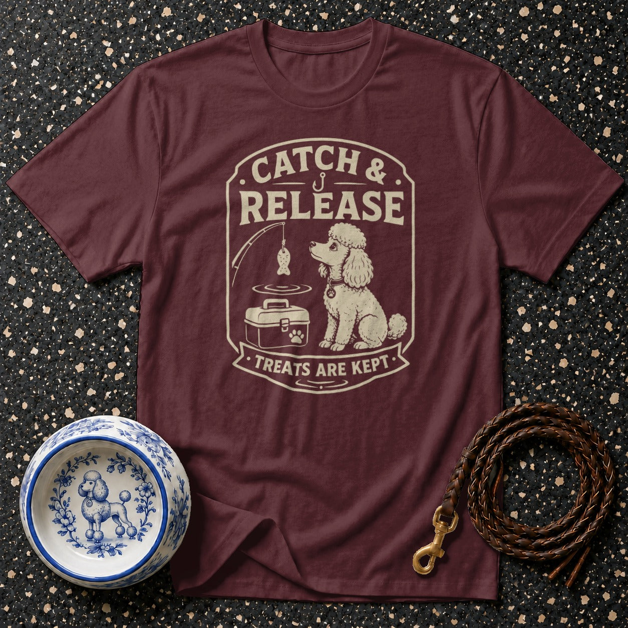 T-shirt with cream graphic of poodle, fishing pole, tackle box, and text "Catch & Release Treats Are Kept".