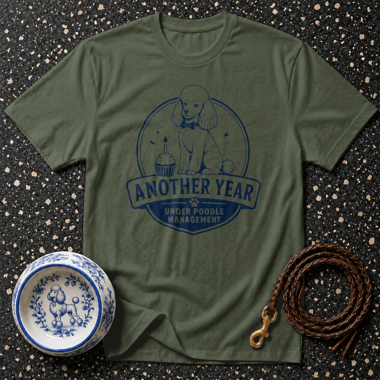 Olive green t-shirt with blue poodle graphic and text: "Another Year Under Poodle Management".