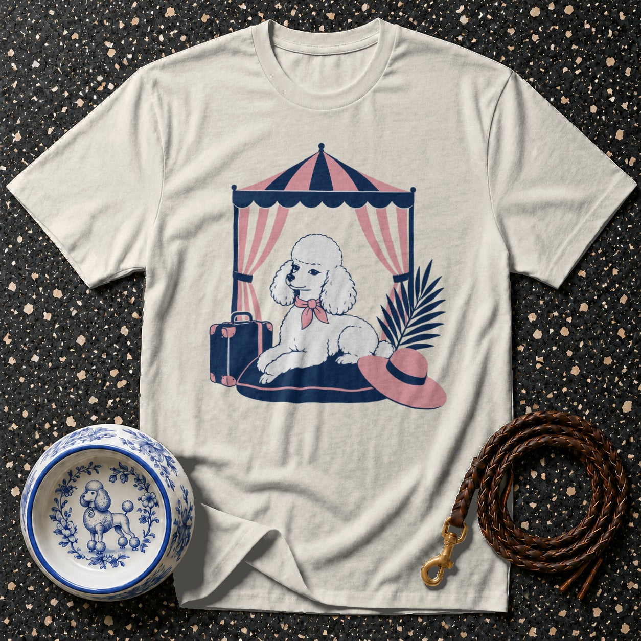 White t-shirt with a graphic of a poodle under a striped tent, next to a suitcase.