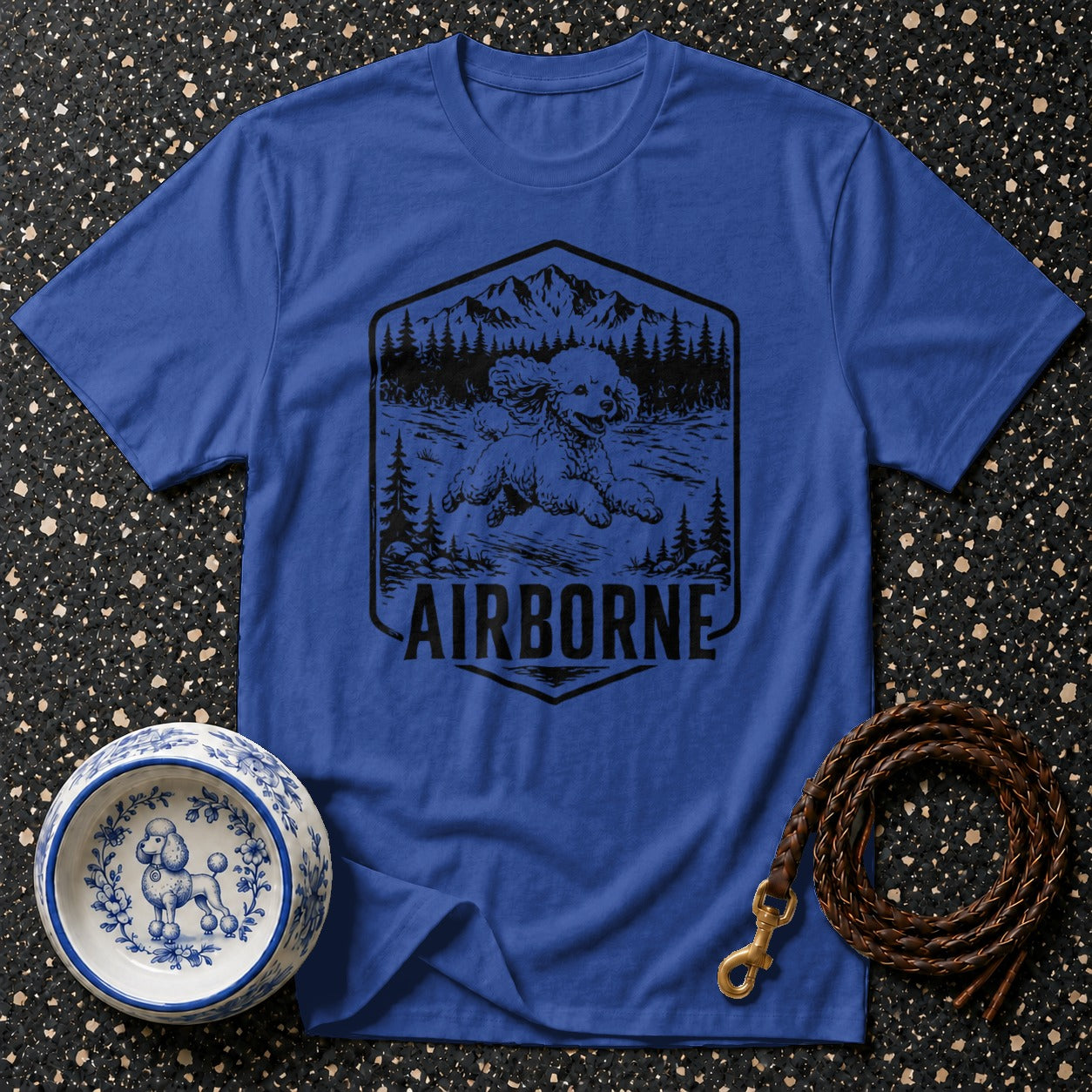 Blue t-shirt with a black graphic of a poodle in a mountain scene with "AIRBORNE" text.