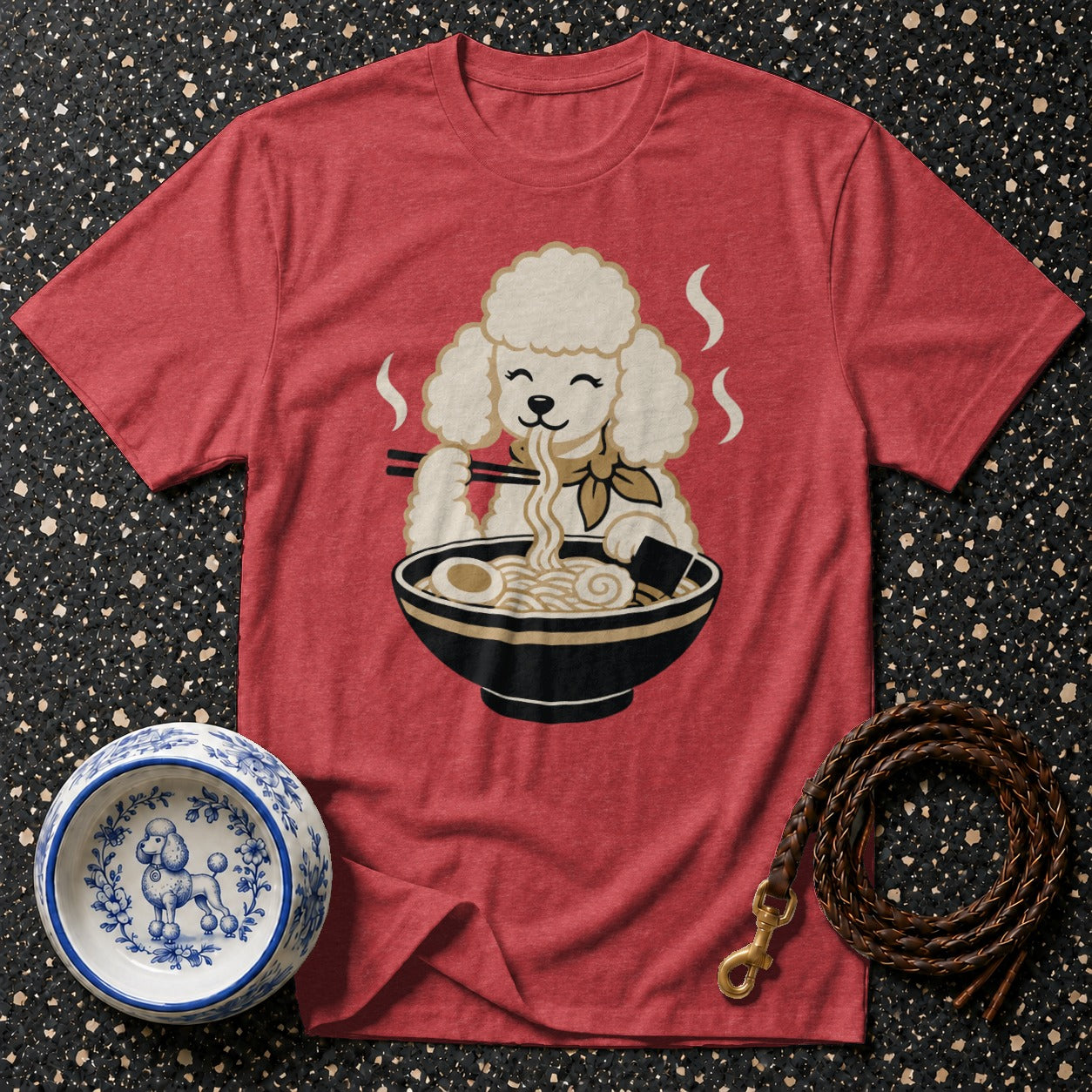 Red t-shirt with a cartoon poodle eating ramen, near a decorative dog bowl and leash.