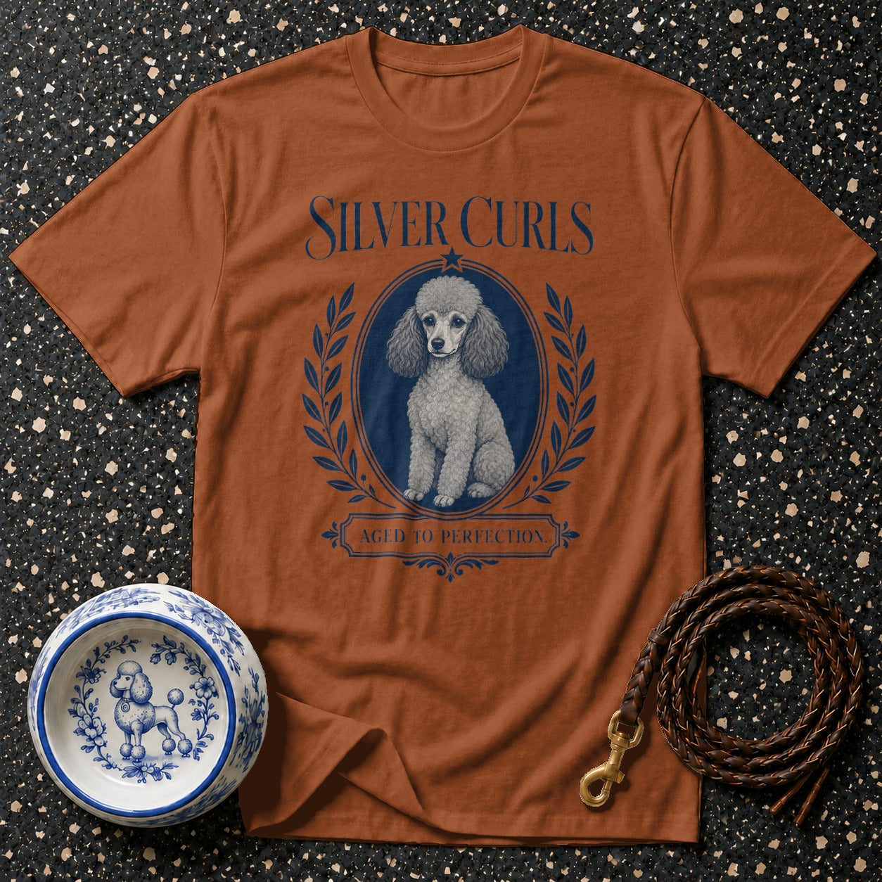 Brown t-shirt with "Silver Curls" and poodle graphic, next to a decorative dog bowl and leash.