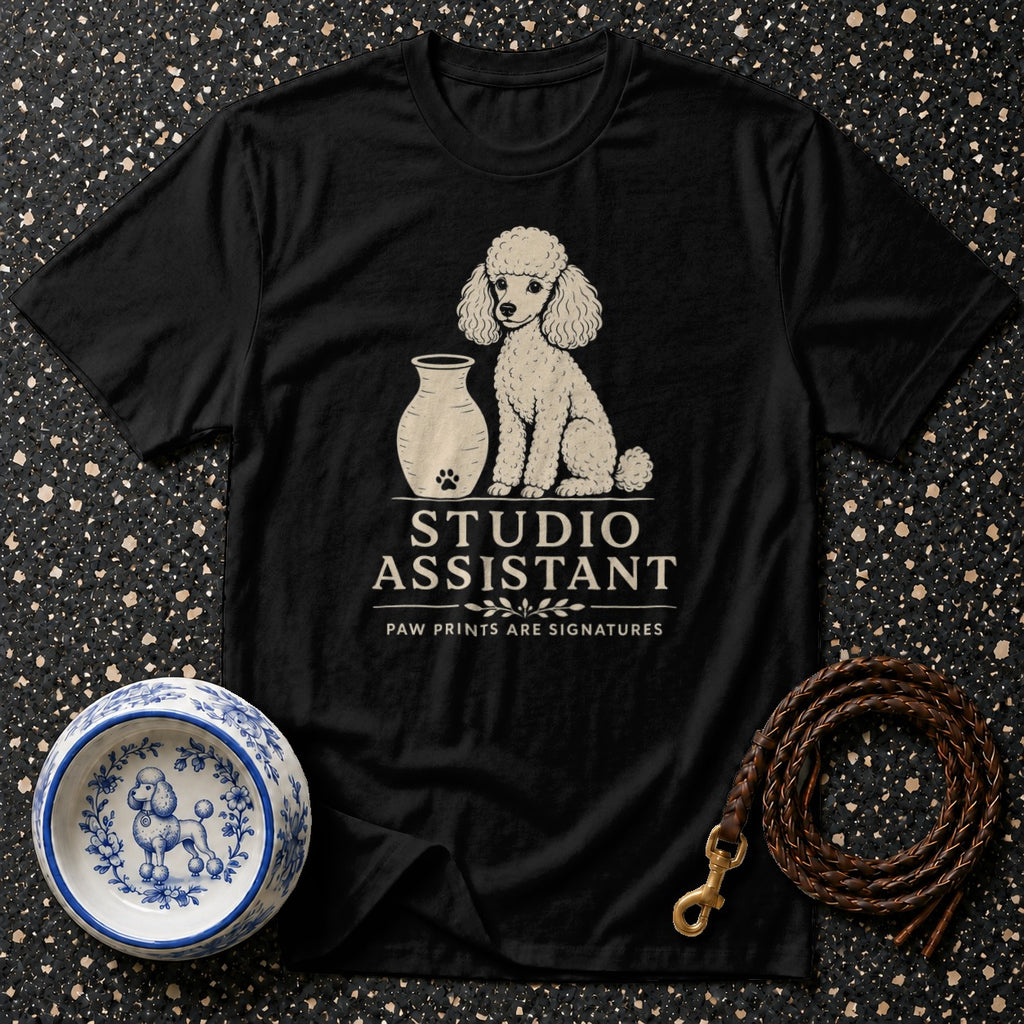 Black t-shirt with white poodle graphic, vase, and text "STUDIO ASSISTANT".