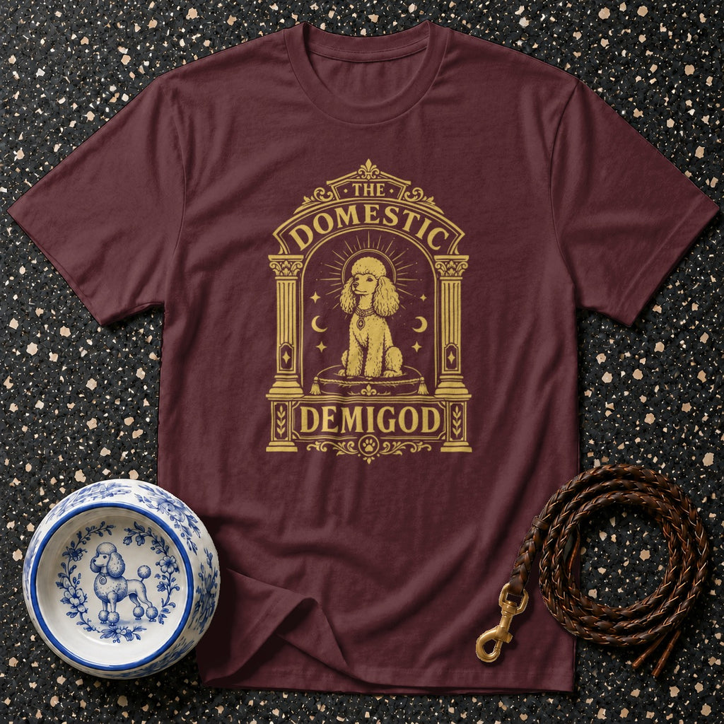 Maroon t-shirt with a gold poodle graphic that reads "THE DOMESTIC DEMIGOD".