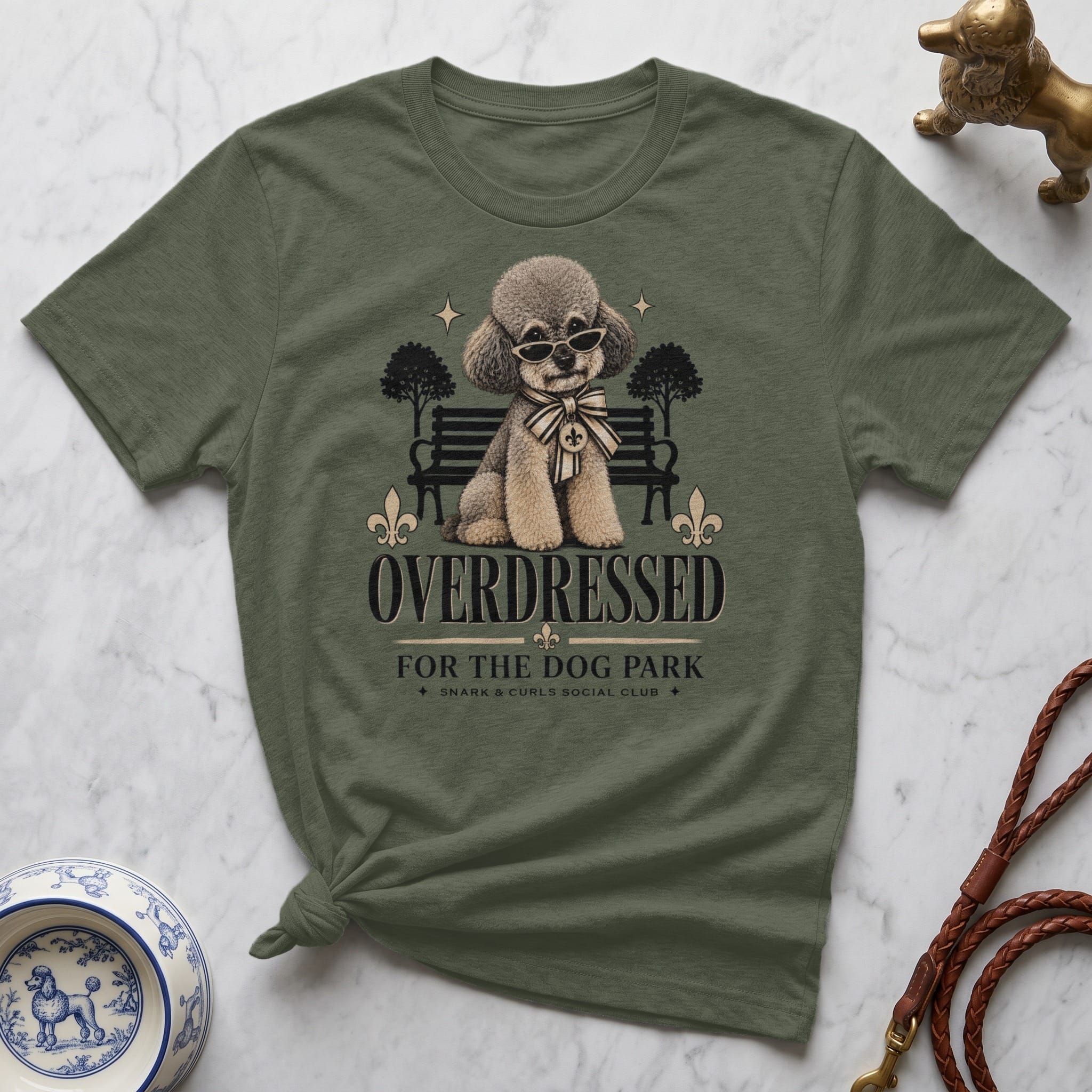 Olive green t-shirt with poodle illustration, sunglasses, and "Overdressed" text.
