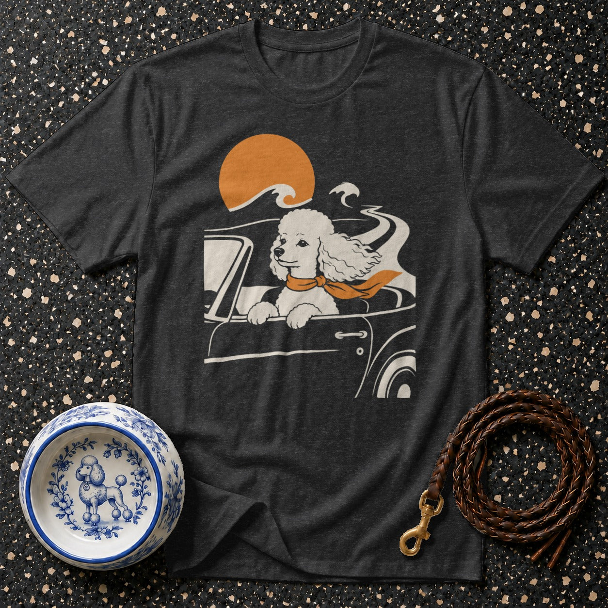 Poodle driving a car with orange scarf and sunset graphic on dark gray t-shirt.